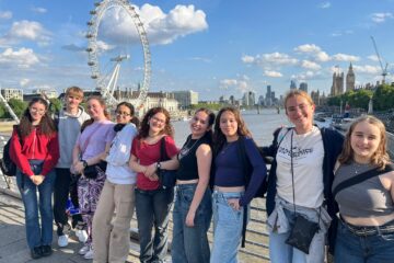 Groupe de jeunes adultes posant devant le London Eye et la Tamise à Londres, avec des bâtiments en arrière-plan.