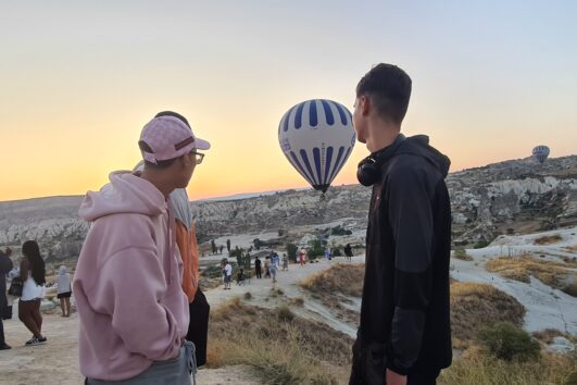 Au lever du soleil, des voyageurs observent des montgolfières survolant les formations rocheuses de la Cappadoce, en Turquie.